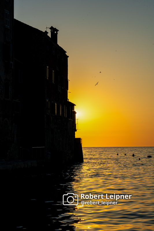 Sonnenuntergang hinter einer Häuserzeile am Wasser nahe des Hafens